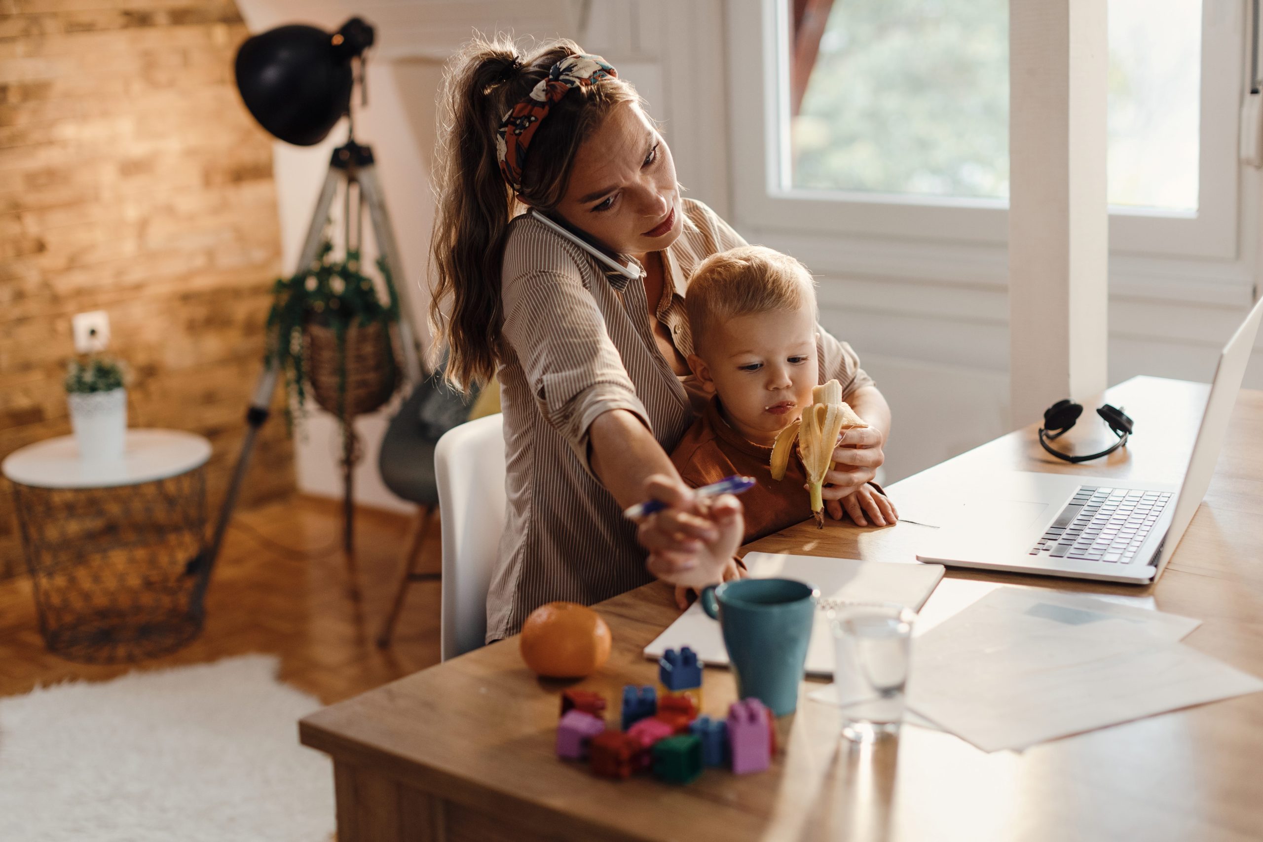 mulher, mãe, a segurar um bebé enquanto está ao telefone, a trabalhar e a alimentar o filho. Mulher atarefada em multitasking.